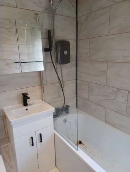 A bathroom finished with a bath screen, vanity unit and black fittings