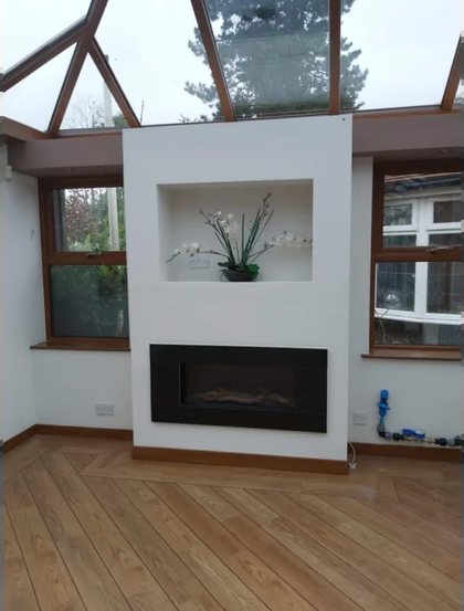 A conservatory finished inside, with a pitched timber roof and a built in fireplace wall