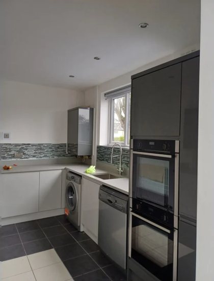 A fitted kitchen with grey gloss units, a double oven and a mosaic splashback