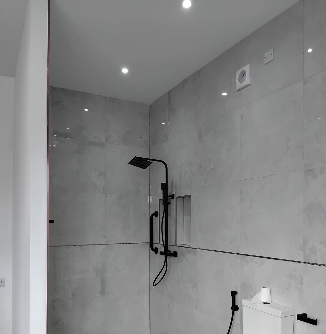 A level access walk in wet room with a black rainfall shower, grab rail and a tiled niche